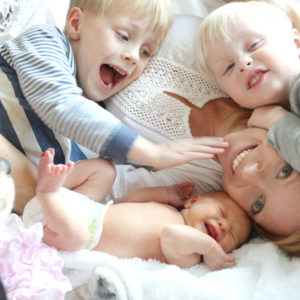 Happy Young Mother And Three Children Snuggling On Bed
